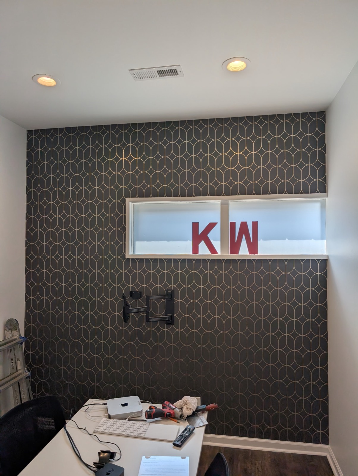 Office feature wall finished in dark geometric wallpaper with a gold pattern