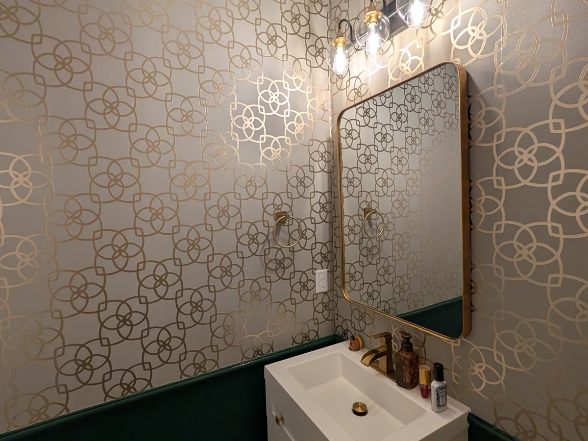 Powder room — gold geometric paper above deep green wainscot